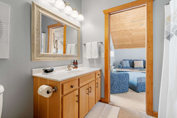 Interior view of a modern bathroom with wooden elements and a doorway leading to a blue-upholstered seating area.