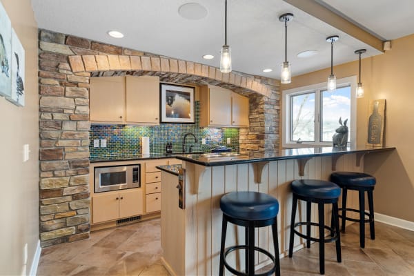 Modern kitchen with bar area, stone arch, pendant lights, and colorful tile backsplash.