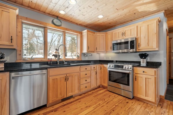 A kitchen featuring wooden cabinetry, black granite countertops, and stainless steel appliances, illuminated by natural light from large windows.