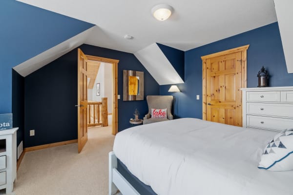 A bedroom with navy blue walls, a white bed, and rustic wood details.