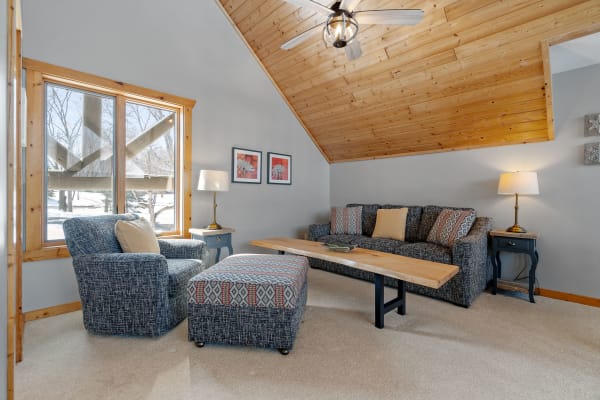 Cozy living room with a wooden ceiling, comfortable seating, and a large window with outdoor views.