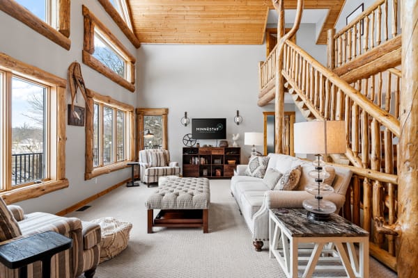 Spacious living area in a log cabin with a high ceiling and large windows.