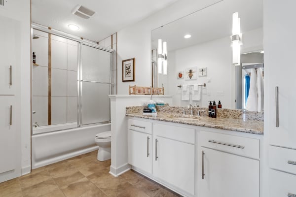 A contemporary bathroom featuring a granite vanity and glass shower enclosure.