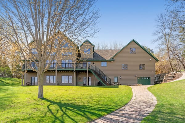 Large brown house with green accents and expansive windows, set in a green landscape with a winding brick pathway.