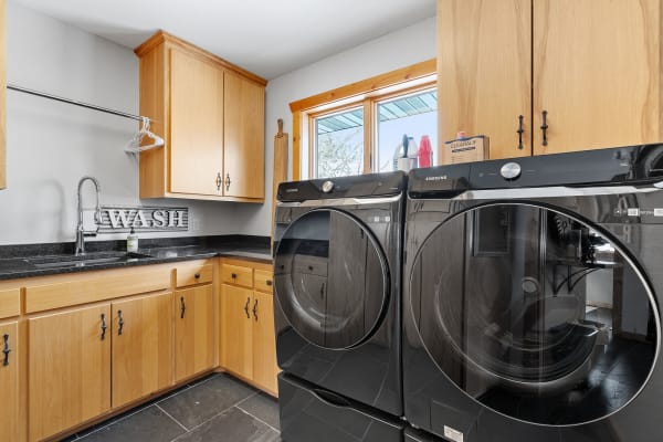 Modern laundry room featuring black washing machines and wooden cabinets.