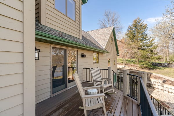 A wooden porch area with rocking chairs and a view of trees and water.