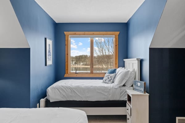 A serene bedroom with blue walls, twin beds, and a large window overlooking a calm landscape.