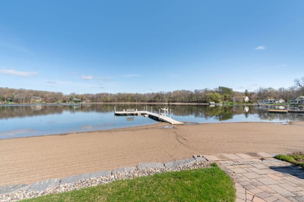 Tranquil lakeside scene with a sandy beach and wooden dock under a blue sky.