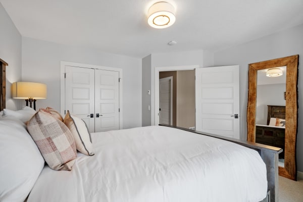 A modern bedroom with white bedding, decorative pillows, and a wood-framed mirror.