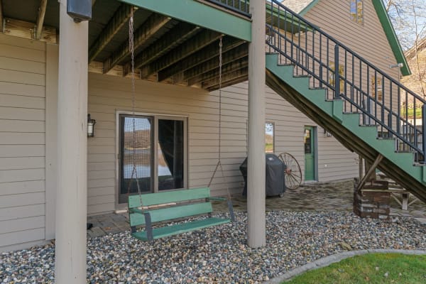 Outdoor area featuring a green swing, pebbled ground, and a staircase next to a house.