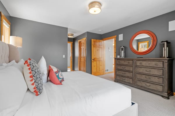 Bedroom featuring a gray wall, white bed, decorative pillows, and a wooden dresser with a mirror.