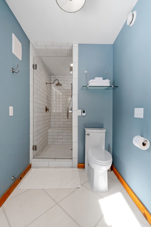 Modern bathroom with blue walls, white tile shower, and shelf of towels.