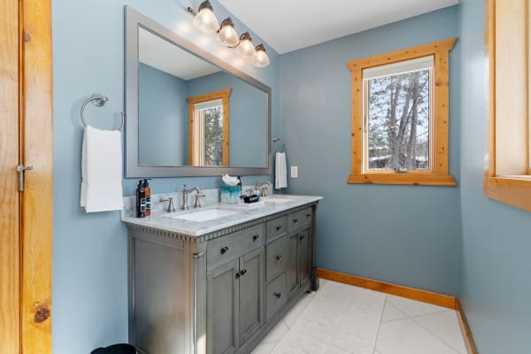 Modern bathroom with gray vanity, blue walls, natural light from window, and wooden accents.