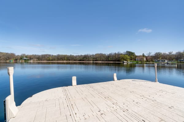 A serene lake view featuring a wooden dock and lush greenery in the background.