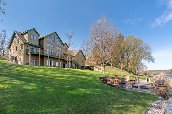 Lakeside house with a green lawn and outdoor seating area.