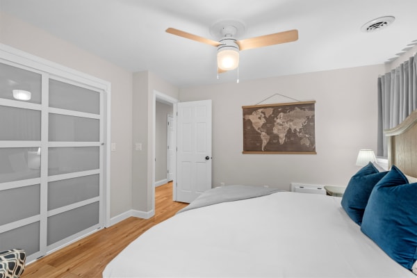 A cozy bedroom with a white bed, turquoise pillows, a ceiling fan, and a world map on the wall.