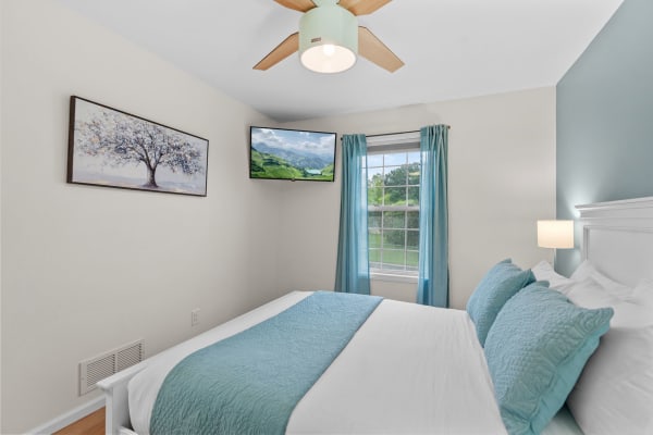 Cozy bedroom featuring a queen-size bed, blue pillows, and a mounted TV displaying a scenic landscape.