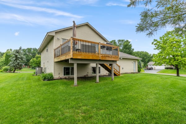 Side view of a two-story house with an elevated deck and green lawn.