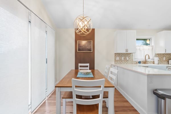 A modern dining area with a wooden table and white chairs, illuminated by a spherical chandelier.