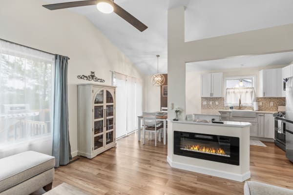 A modern living space featuring a dining area, electric fireplace, and kitchen, with warm wooden flooring and soft curtains.