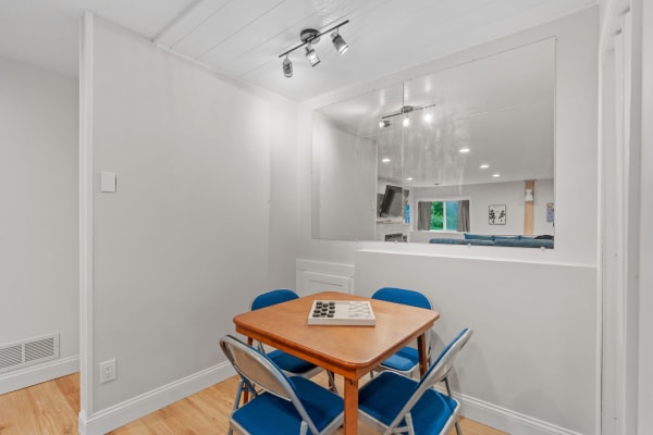 A small dining area featuring a wooden table, blue chairs, and a checkers game set on the table.