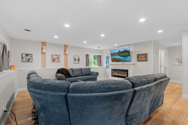A living room featuring a blue sectional sofa, a modern fireplace, and a wall-mounted TV displaying a mountain lake scene.