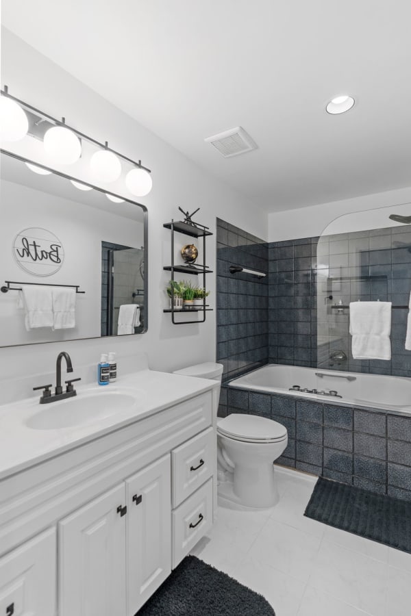 A contemporary bathroom with a white vanity, black fixtures, and blue tiled bathtub area.