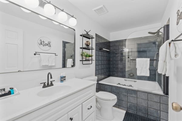 A contemporary bathroom with a white vanity, glass shower, and decorative shelving.