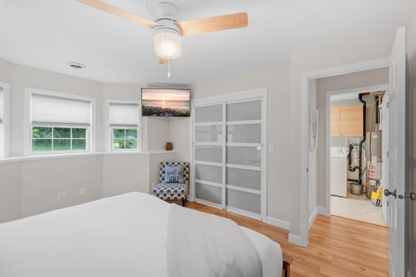 A bright bedroom with a bed, ceiling fan, TV showing a sunset, and a chair in the corner.
