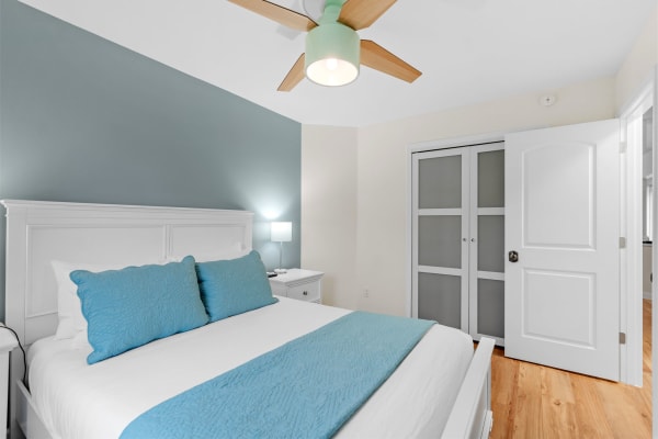 A serene bedroom with a white bed, turquoise pillows, and a mint green ceiling fan.