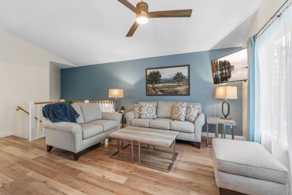 A comfortable living room with light gray sofas, a wooden coffee table, a blue wall, and a modern lamp.