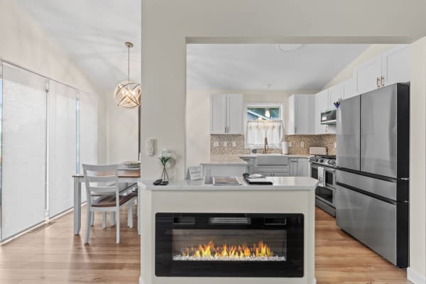 A modern kitchen featuring white cabinets, a dining nook, and an electric fireplace.