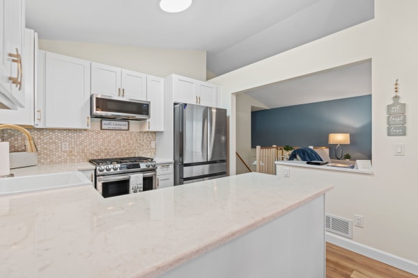 Contemporary kitchen featuring white cabinets, stainless steel appliances, and a stylish living room in the background.