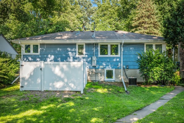A single-story blue house with a white gate, green grass, and trees in the background.