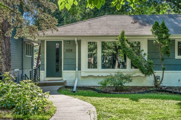 A single-story home with a green door, large windows, and a curved pathway lined with plants.