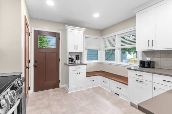A modern kitchen featuring a corner bench, sleek cabinetry, and large windows overlooking greenery.