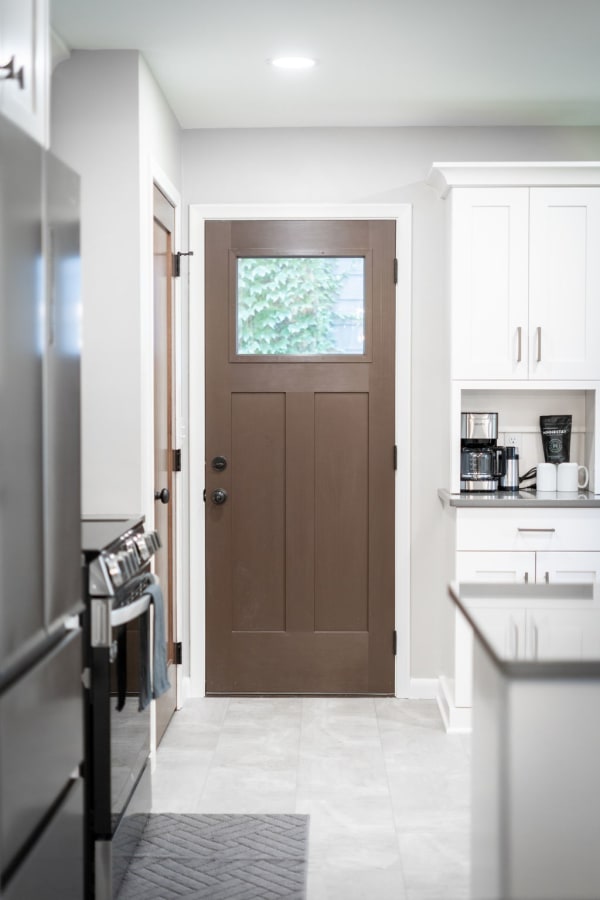 A contemporary kitchen interior with a brown front door and white cabinets, highlighting a coffee setup.