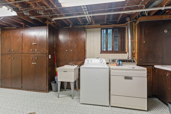 Basement laundry area with wooden cabinets, washing machine, dryer, and laundry sink.