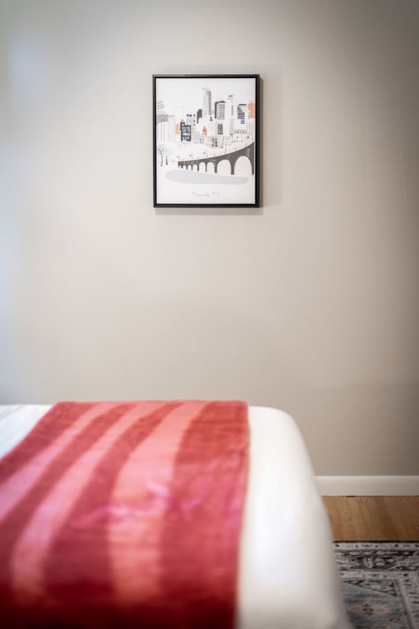 A bedroom with a red-striped blanket and a framed artwork of Minneapolis on the wall.