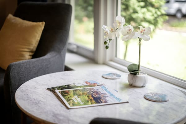 A round marble table with magazines and a white orchid in a pot, beside a gray armchair.