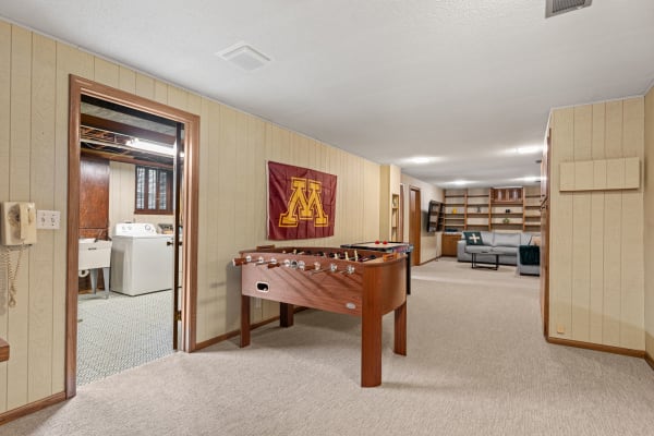 A spacious basement with a foosball table, laundry area, and seating space.