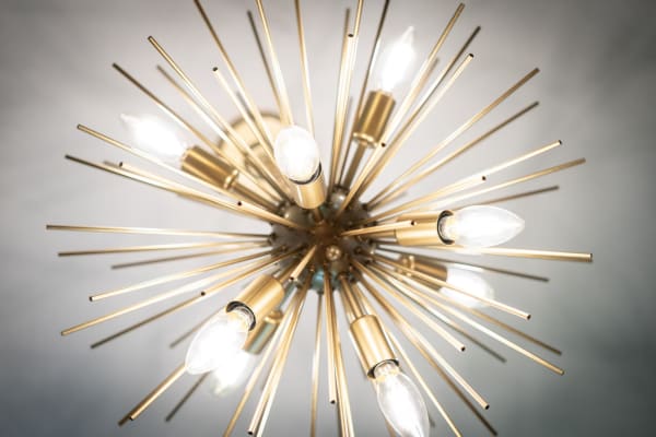 A contemporary chandelier designed in a starburst shape with gold rods and illuminated bulbs.