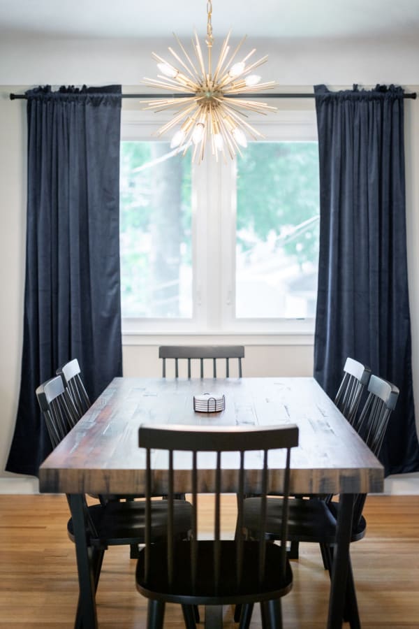 Interior view of a dining room with a wooden table, black chairs, and a golden chandelier.