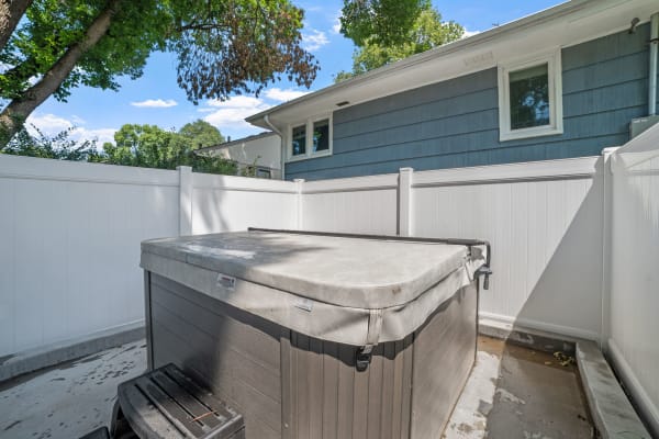 An outdoor hot tub surrounded by a white fence with a blue house in the background.