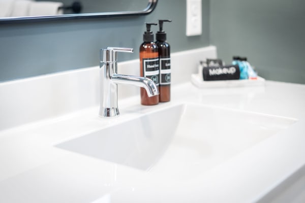 Close-up of a chic bathroom sink featuring a chrome faucet and brown soap bottles on a white countertop.