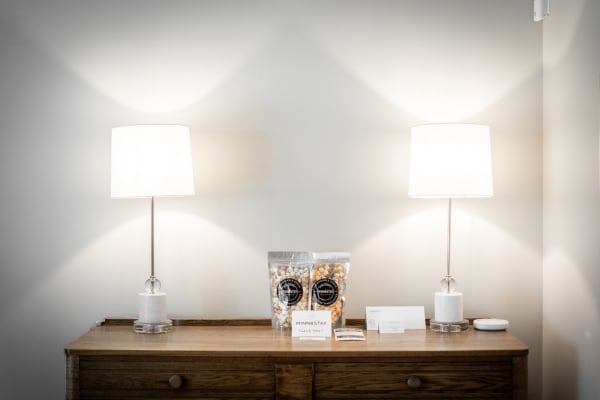A minimalist bedside table with two lamps, a bag of popcorn, and a thank-you card.