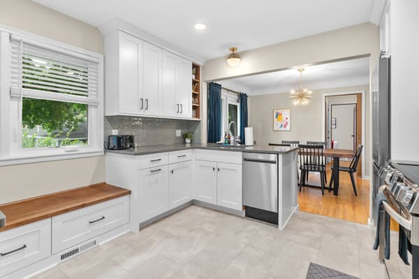 Modern kitchen featuring white cabinets, a wooden bench, and a dining area.