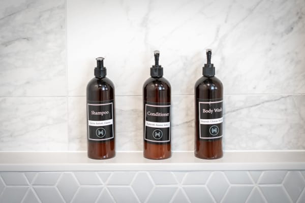 Three dark amber bottles labeled Shampoo, Conditioner, and Body Wash on a marble ledge.