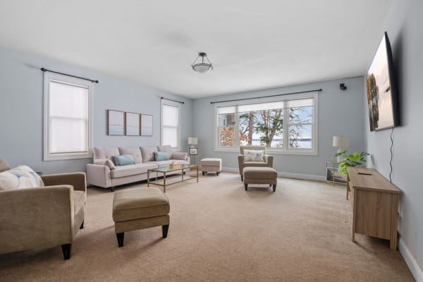 A modern living room featuring a soft pink sofa, beige armchair, and large windows with natural light.