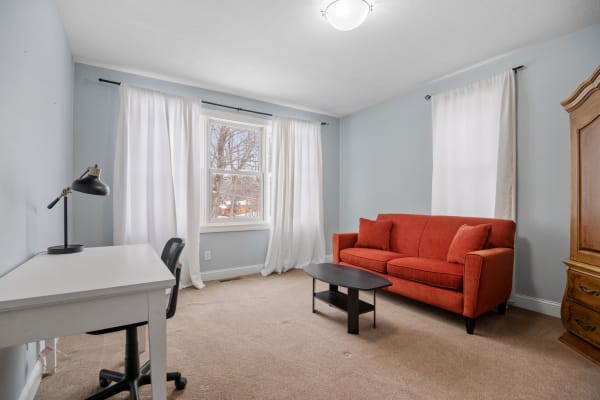 Cozy living room featuring an orange sofa, a black coffee table, and a white desk with a chair.